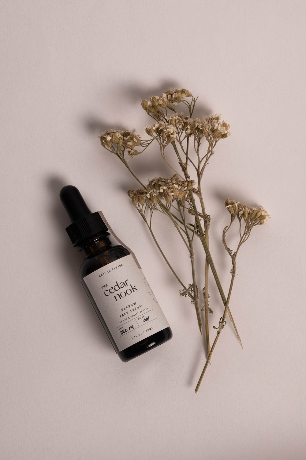 The Cedar Nook | Yarrow Face Serum for dry and sensitive skin in our 1 oz amber glass bottle, laying flat surrounded by dried foraged yarrow flowers