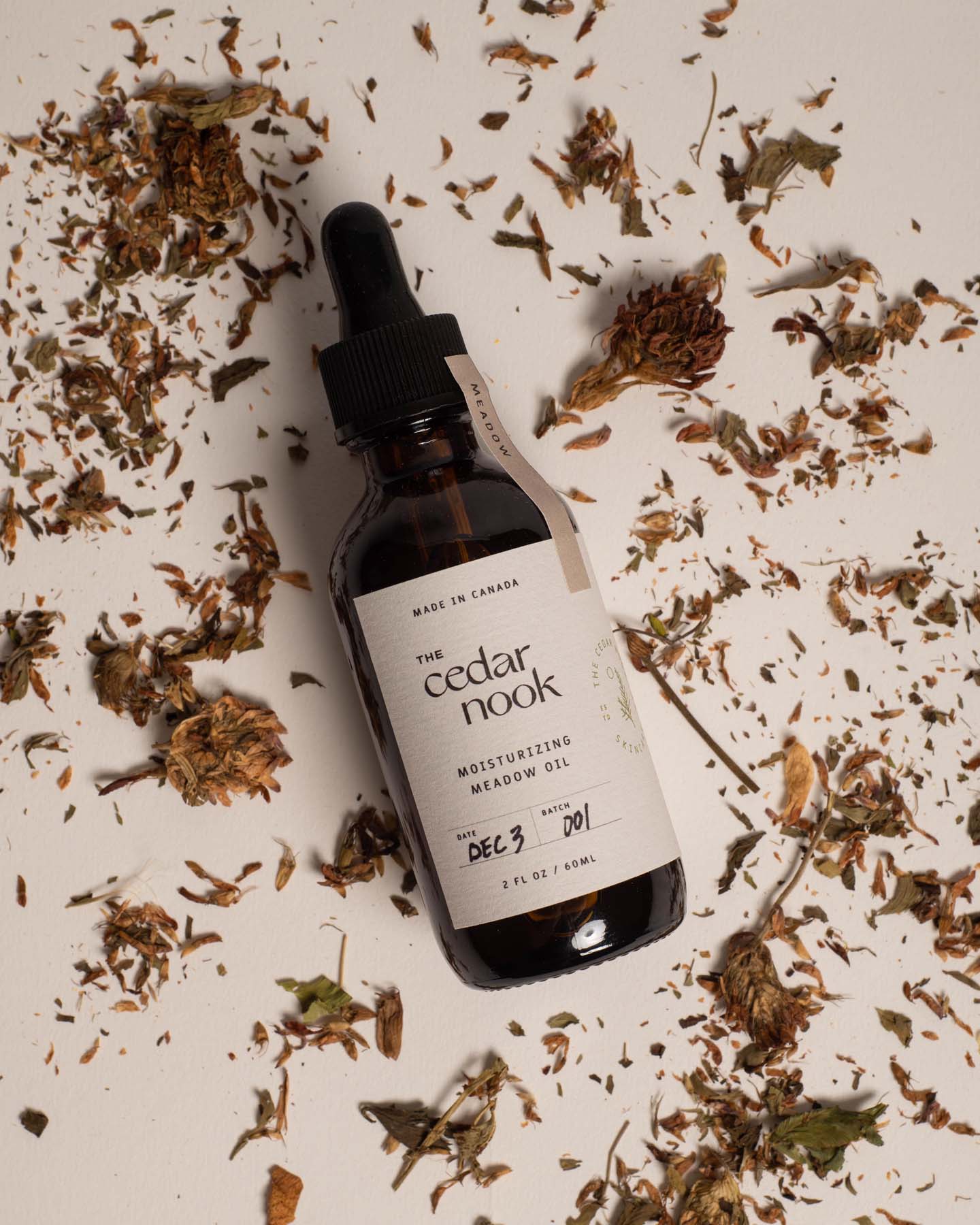 Moisturizing Meadow Oil | The Cedar Nook Face Oil in a 2 oz amber glass bottle with dropper top in a flat lay view and foraged red clover blossoms sprinkled all around a white background
