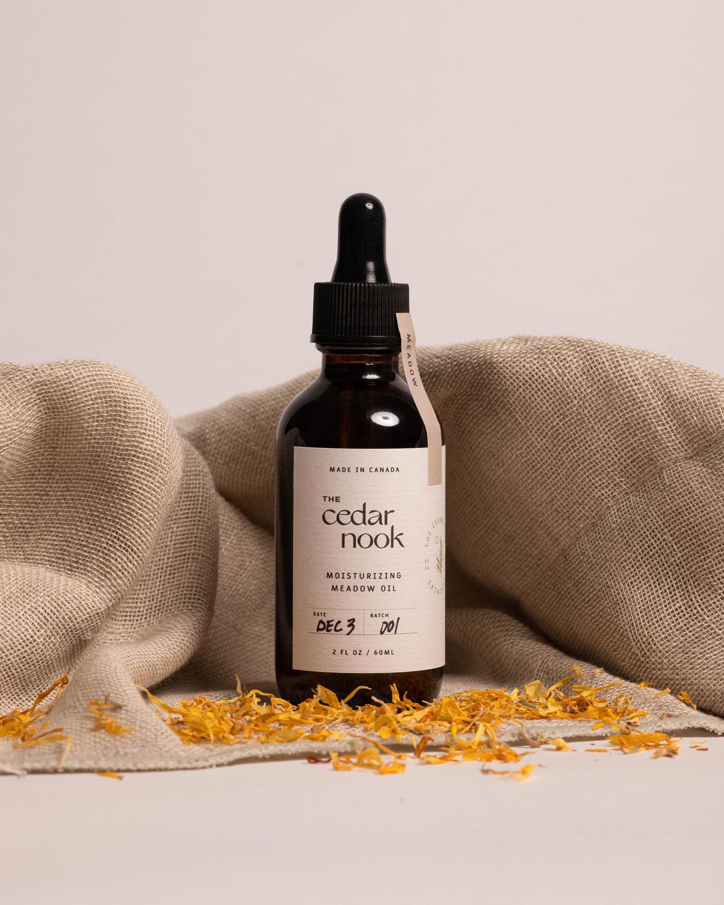 Moisturizing Meadow Oil | The Cedar Nook Face Oil in a 2 oz amber glass bottle with dropper top standing in front of a linen towel and dried calendula leaves