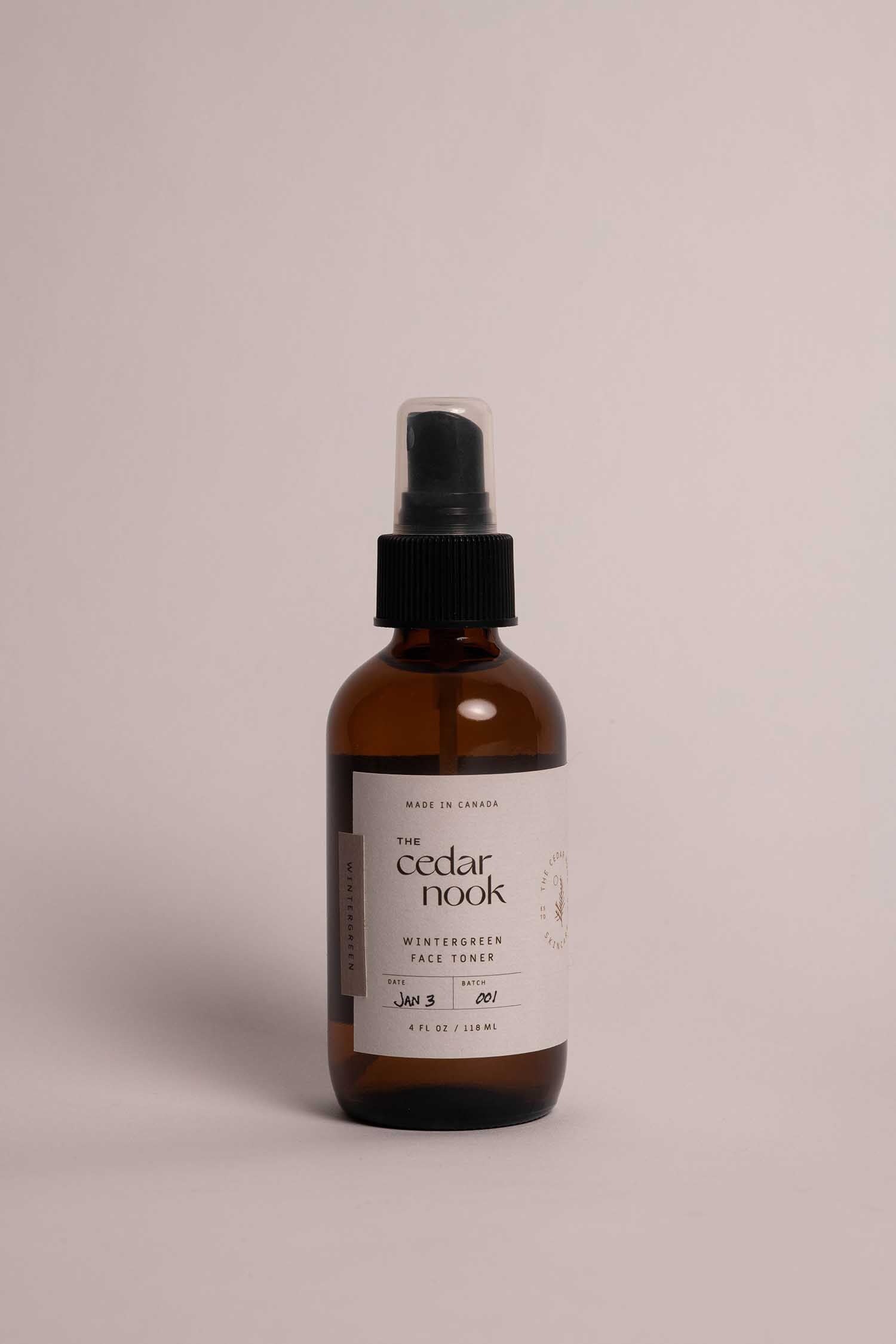 The Cedar Nook Wintergreen Face Toner in a 4 oz amber glass bottle with a spray top, standing alone on a white background, showing the front white label with forest green logo