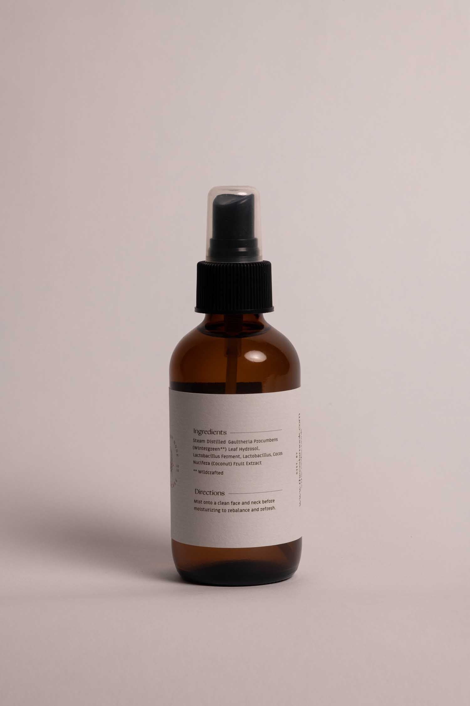 The Cedar Nook Wintergreen Face Toner in a 4 oz amber glass bottle with mist top back view, showing white label with list of ingredients and directions for use